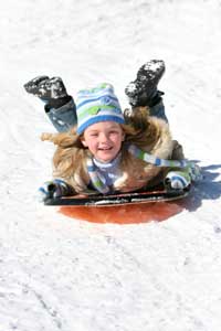 girl sliding down snow hill on suacer