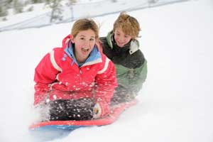 two kids sliding down snow hill on suacer